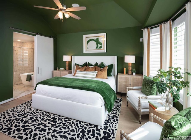 bedroom with ceiling fan, light hardwood / wood-style flooring, a barn door, connected bathroom, and vaulted ceiling