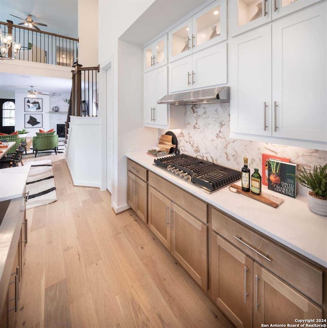 kitchen featuring backsplash, white cabinets, stainless steel gas cooktop, ceiling fan, and light hardwood / wood-style flooring