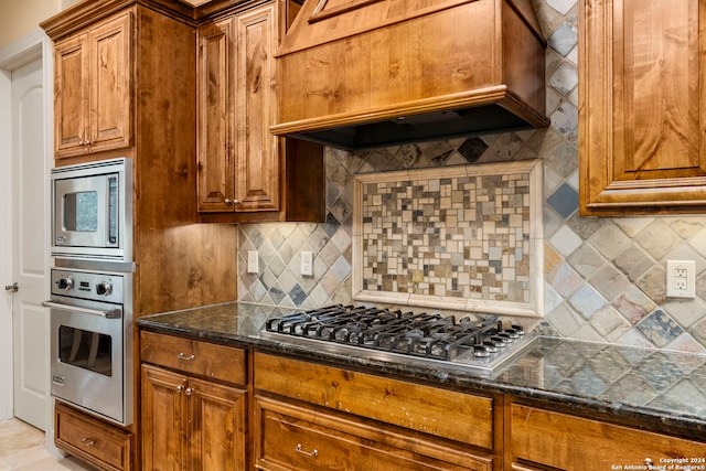 kitchen with custom range hood, appliances with stainless steel finishes, tasteful backsplash, and dark stone countertops