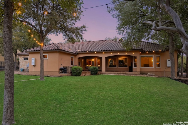 back house at dusk featuring a lawn