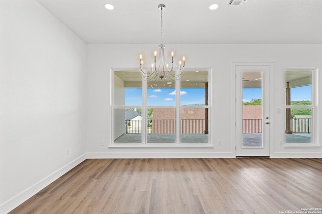 unfurnished dining area with a chandelier, light wood-type flooring, and plenty of natural light