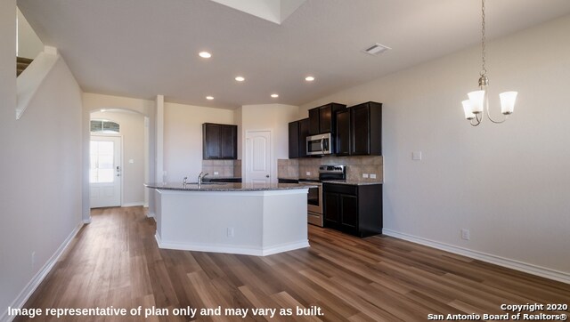 kitchen with tasteful backsplash, stainless steel appliances, pendant lighting, dark hardwood / wood-style floors, and a kitchen island with sink