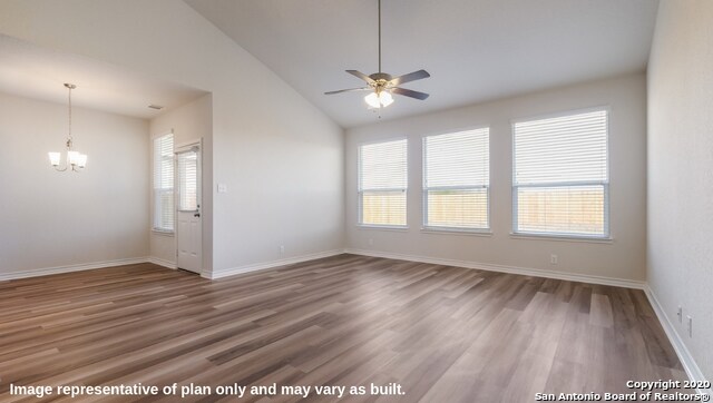 empty room featuring ceiling fan with notable chandelier, wood-type flooring, and plenty of natural light