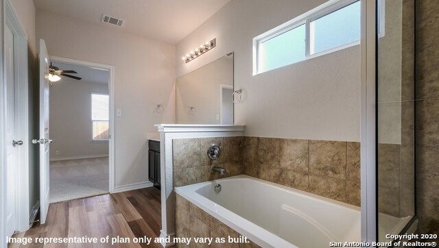 bathroom featuring vanity, a relaxing tiled tub, plenty of natural light, and hardwood / wood-style floors