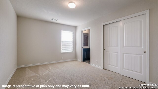 unfurnished bedroom featuring ensuite bathroom, light colored carpet, and a closet