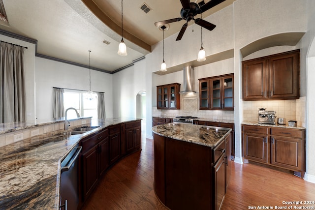 kitchen with appliances with stainless steel finishes, wall chimney exhaust hood, hardwood / wood-style flooring, and an island with sink