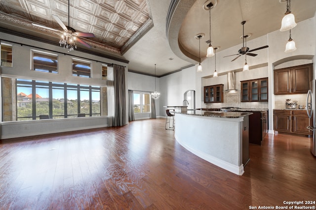 kitchen featuring a kitchen island with sink, dark hardwood / wood-style floors, dark stone countertops, decorative light fixtures, and a towering ceiling