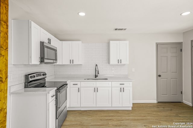 kitchen with backsplash, sink, light wood-type flooring, white cabinetry, and stainless steel appliances