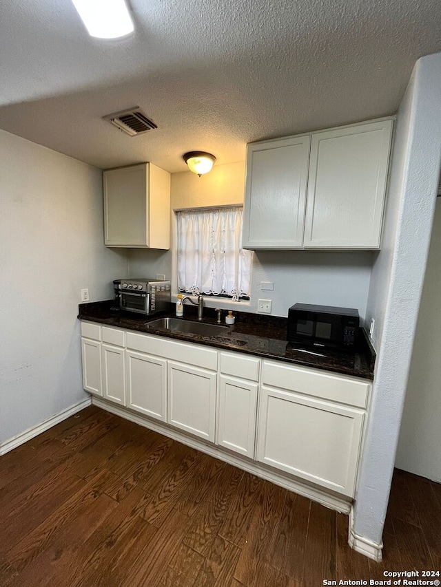 kitchen with a textured ceiling, white cabinets, sink, and dark hardwood / wood-style flooring