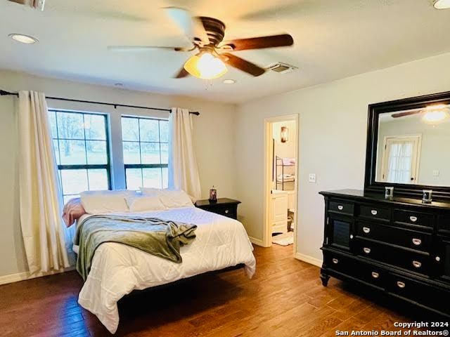 bedroom with connected bathroom, ceiling fan, and dark hardwood / wood-style flooring