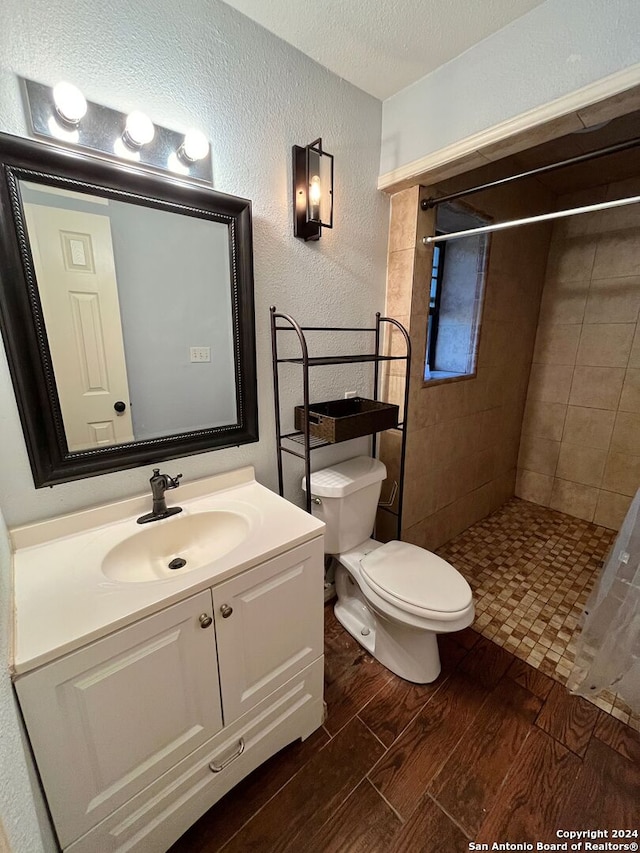 bathroom featuring toilet, a textured ceiling, vanity, and tiled shower