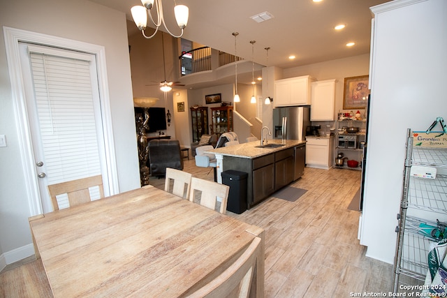 dining area with light wood-type flooring, ceiling fan with notable chandelier, and sink