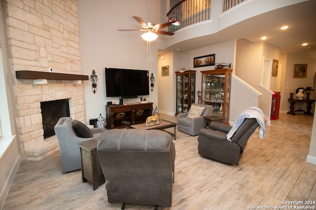 living room featuring a fireplace, a towering ceiling, light hardwood / wood-style floors, and ceiling fan