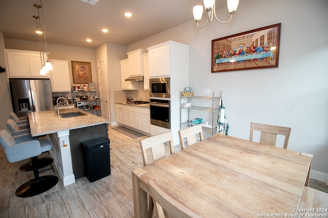 kitchen with stainless steel appliances, sink, pendant lighting, a center island with sink, and white cabinetry