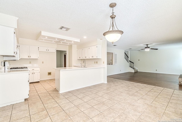 kitchen with a textured ceiling, decorative light fixtures, white cabinets, ceiling fan, and sink