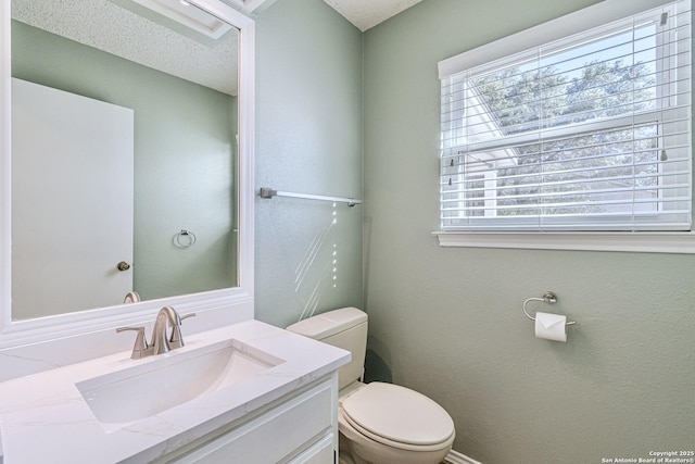 bathroom featuring toilet, vanity, a textured ceiling, and a healthy amount of sunlight