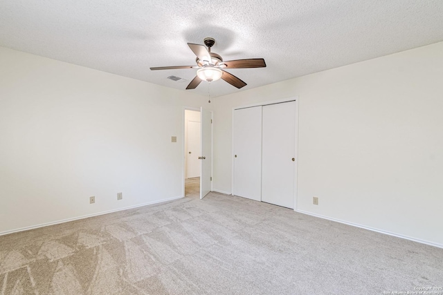 unfurnished bedroom with light colored carpet, ceiling fan, a textured ceiling, and a closet