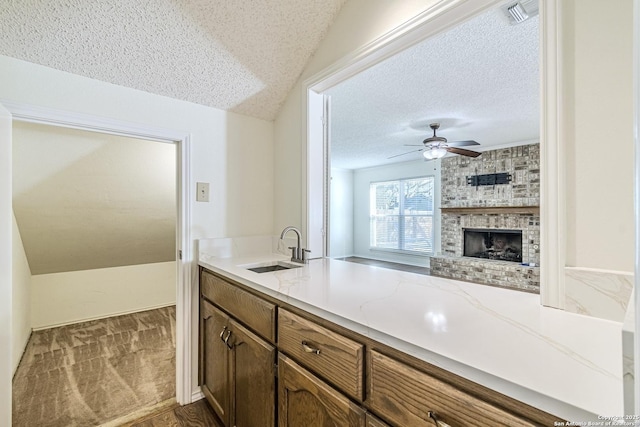 kitchen featuring a textured ceiling, lofted ceiling, a brick fireplace, ceiling fan, and sink