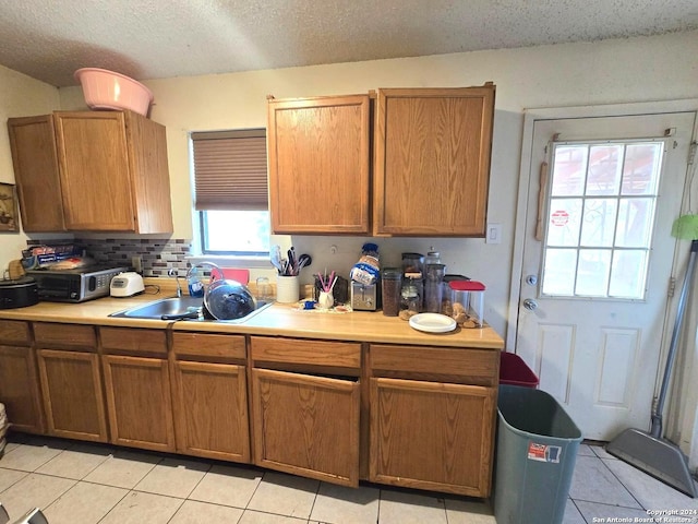 kitchen featuring sink, tasteful backsplash, a textured ceiling, and light tile patterned flooring