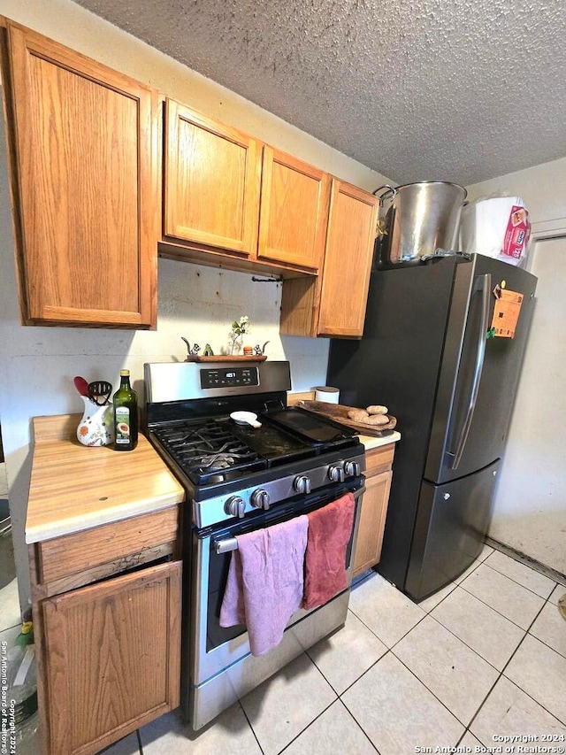 kitchen with a textured ceiling, appliances with stainless steel finishes, and light tile patterned floors