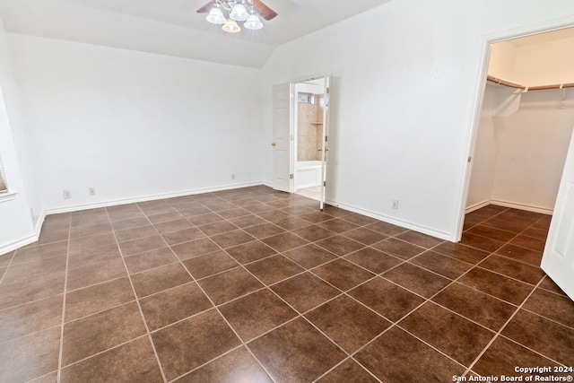 unfurnished bedroom featuring dark tile patterned flooring, a walk in closet, a closet, ceiling fan, and vaulted ceiling