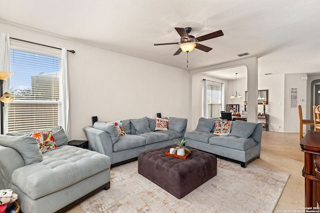 carpeted living room featuring a textured ceiling, plenty of natural light, and ceiling fan with notable chandelier