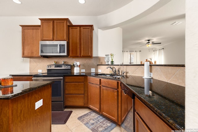 kitchen featuring sink, ceiling fan, stainless steel appliances, dark stone counters, and light tile patterned floors