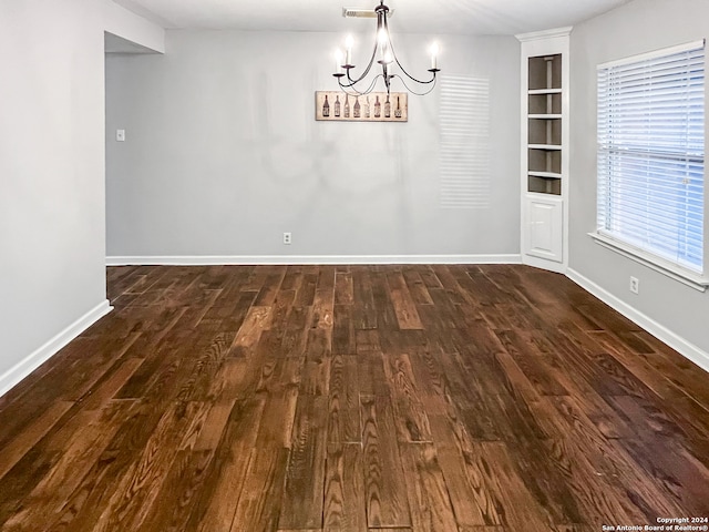 unfurnished dining area with built in features, dark hardwood / wood-style flooring, and a chandelier