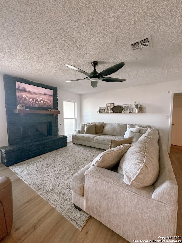 living room with a textured ceiling, a large fireplace, wood-type flooring, and ceiling fan