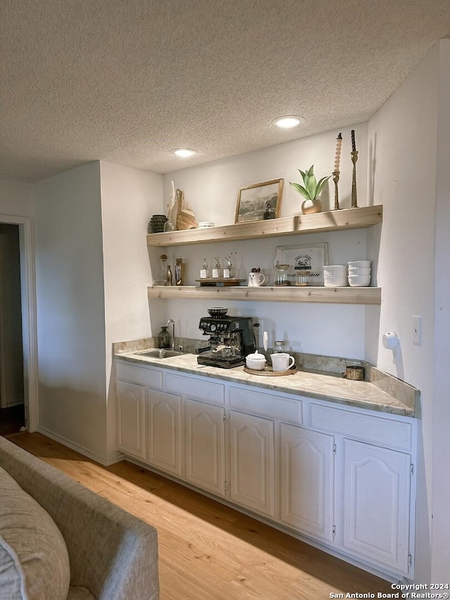 bar with white cabinetry, light hardwood / wood-style flooring, a textured ceiling, and sink