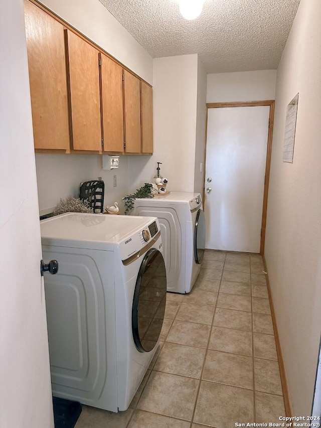 clothes washing area with a textured ceiling, light tile patterned floors, cabinets, and washer and dryer