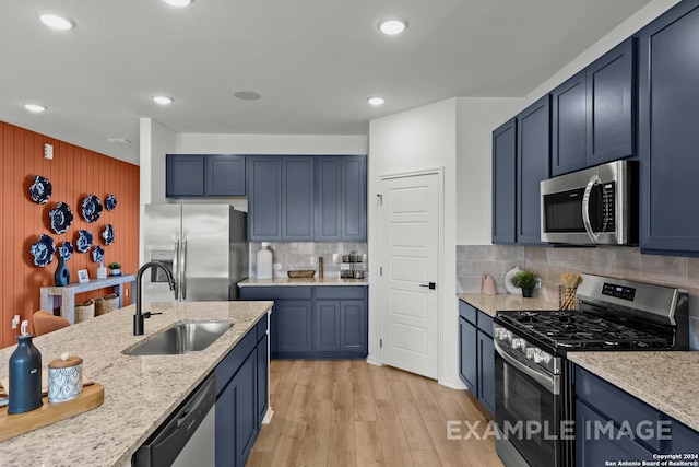 kitchen featuring backsplash, appliances with stainless steel finishes, blue cabinetry, light wood-type flooring, and sink