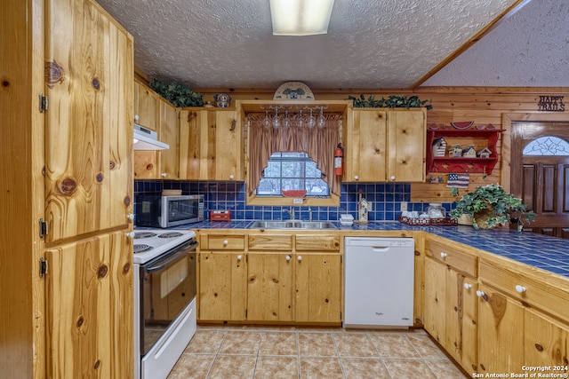 kitchen featuring tile countertops, wooden walls, tasteful backsplash, light tile patterned floors, and white appliances