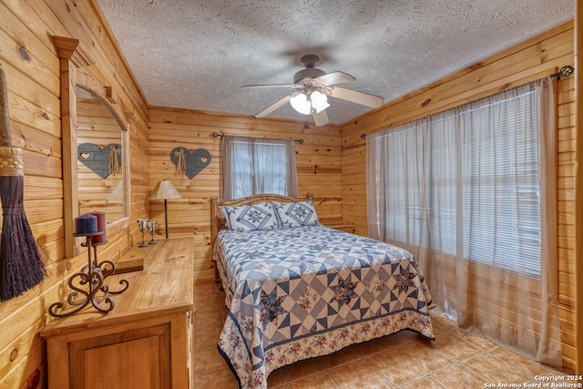 tiled bedroom featuring wood walls, ceiling fan, multiple windows, and a textured ceiling