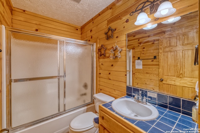 full bathroom with tasteful backsplash, vanity, wood walls, bath / shower combo with glass door, and toilet