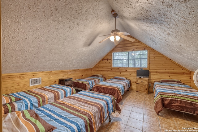 tiled bedroom featuring wood walls, a textured ceiling, ceiling fan, and lofted ceiling