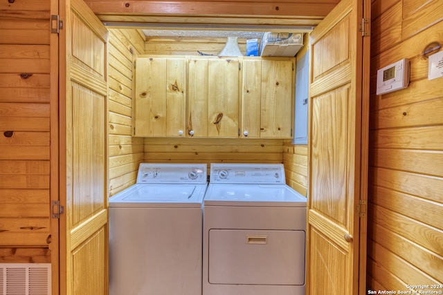 washroom with cabinets, wooden walls, and washing machine and clothes dryer