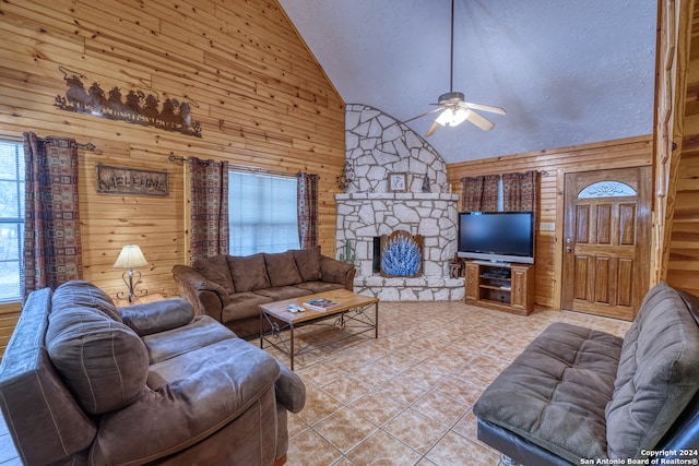 living room featuring ceiling fan, light tile patterned floors, high vaulted ceiling, a fireplace, and wooden walls