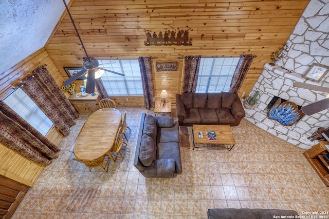 living room with wood walls, wooden ceiling, ceiling fan, light tile patterned floors, and high vaulted ceiling