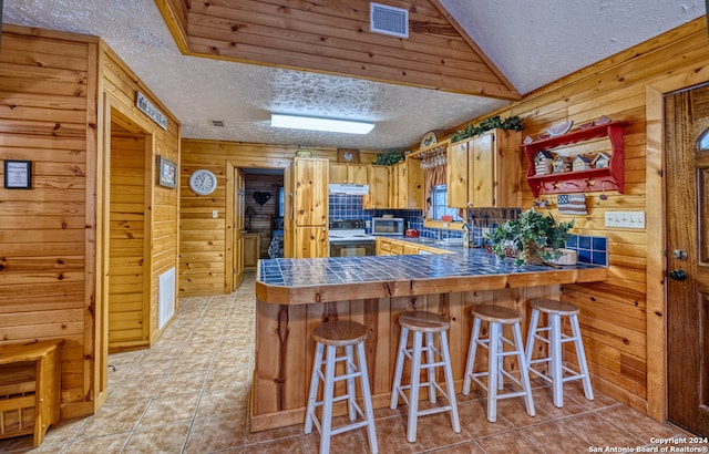 kitchen featuring kitchen peninsula, decorative backsplash, wood walls, a textured ceiling, and a kitchen breakfast bar