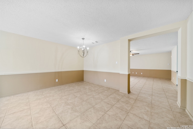 tiled empty room featuring ceiling fan with notable chandelier and a textured ceiling