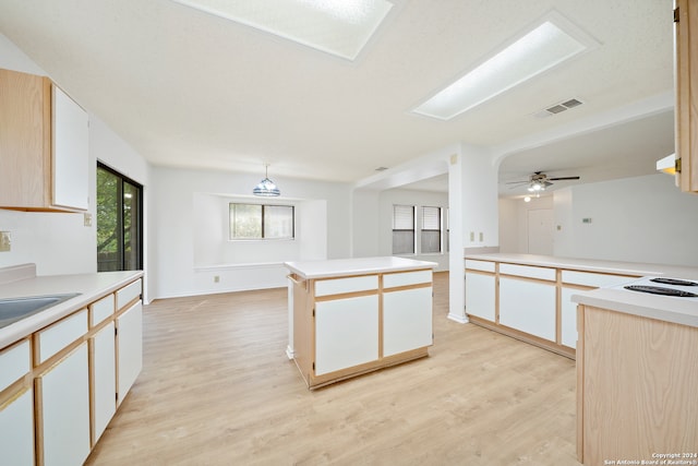 kitchen with a center island, white cabinetry, a skylight, ceiling fan, and light hardwood / wood-style flooring