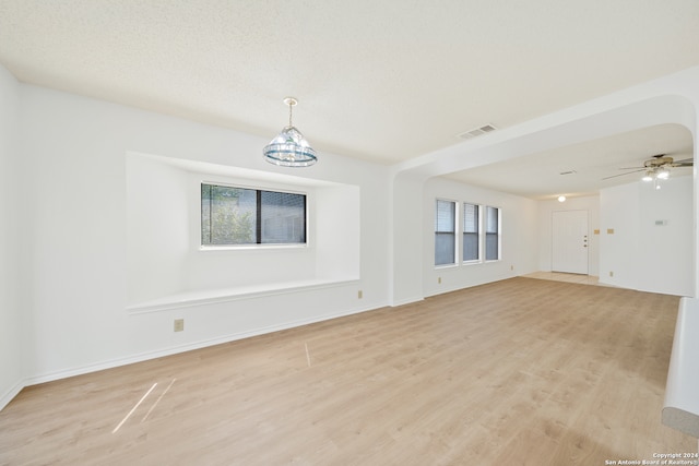 empty room featuring light hardwood / wood-style floors, ceiling fan with notable chandelier, and a textured ceiling