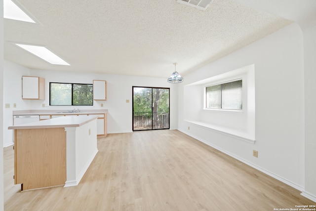 unfurnished living room with sink, a textured ceiling, a skylight, a chandelier, and light hardwood / wood-style flooring