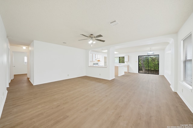 unfurnished living room featuring ceiling fan with notable chandelier, light hardwood / wood-style flooring, and a textured ceiling