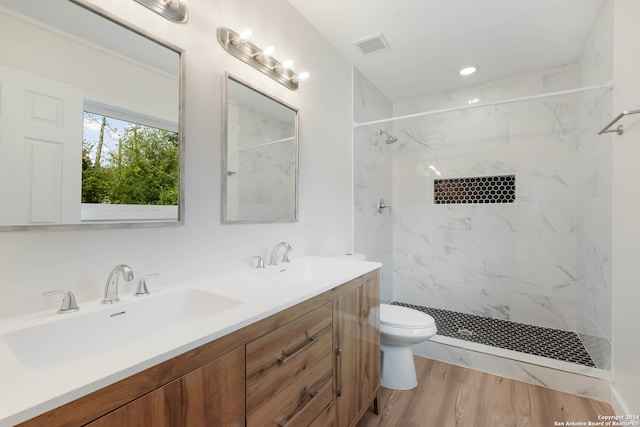 bathroom with toilet, vanity, wood-type flooring, and a tile shower