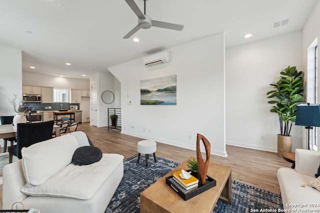 living room featuring light wood-type flooring, a wall unit AC, and ceiling fan