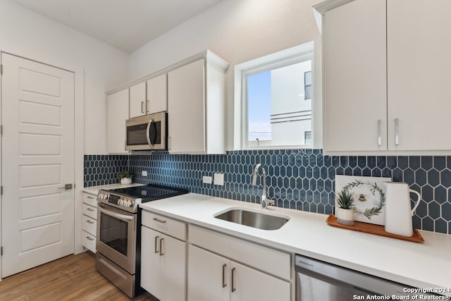 kitchen with stainless steel appliances, light wood-type flooring, white cabinetry, backsplash, and sink