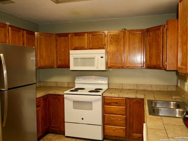 kitchen featuring tile counters, sink, light tile patterned floors, and white appliances