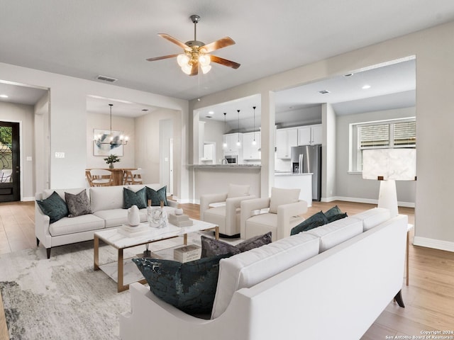 living room featuring light wood-type flooring, a healthy amount of sunlight, and ceiling fan with notable chandelier